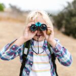 Joyful child using binoculars for outdoor exploration on a sunny day.